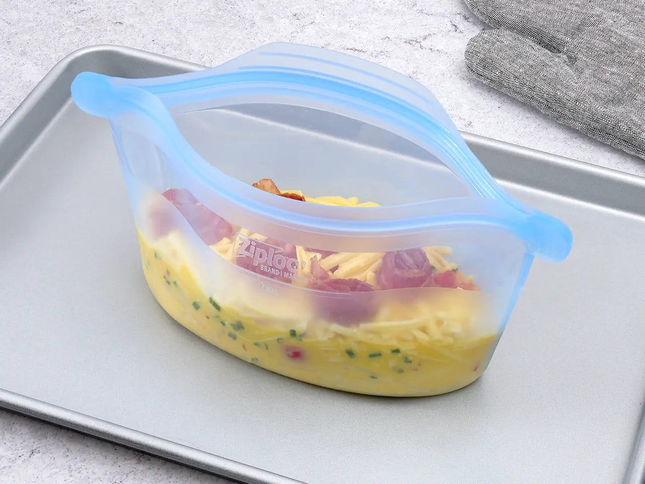 Ziploc Endurables container with potatoes, red pepper, chives, and cheese on baking sheet.