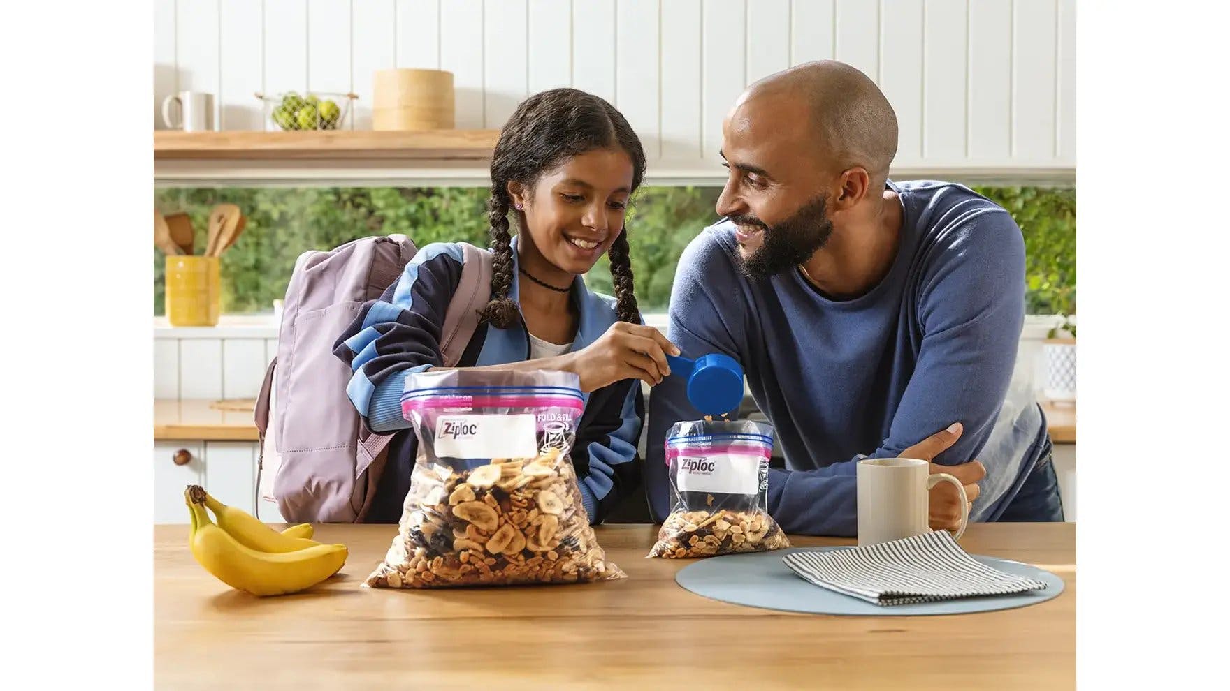 Young girl and man in a kitchen adding trail mix into bags